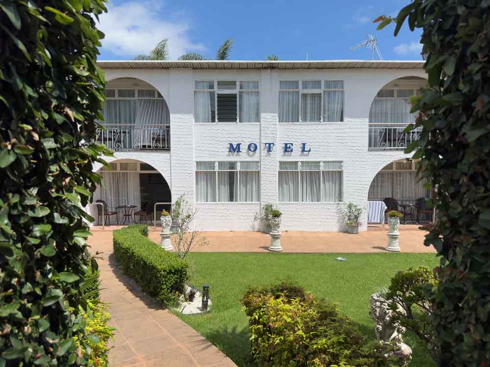 White brick two story exterior of the Aarangi Motel in Mission Bay Auckland framed by green shrubs.