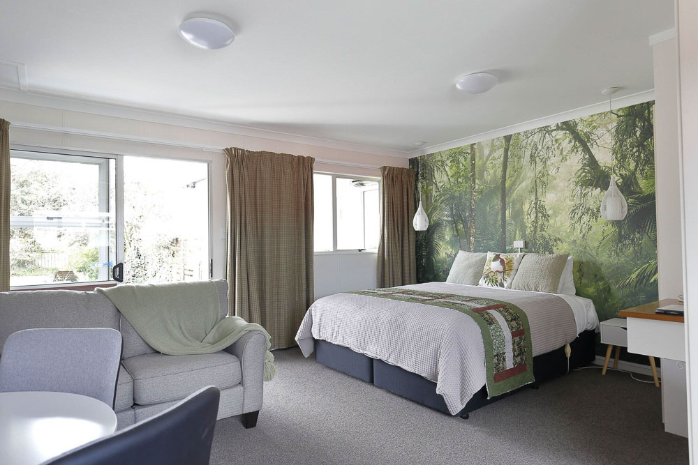 Inside of motel room with bed, green forest wallpaper, a sofa and chairs.