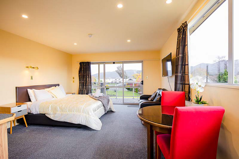 Inside of a motel room with white bed and round table with red chairs