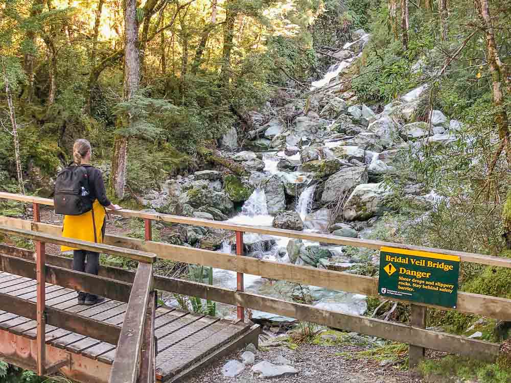 Girl standing on wooden bridge looking at the Cascading Bridal Veil Waterfall on the routeburn track in Glenorchy.