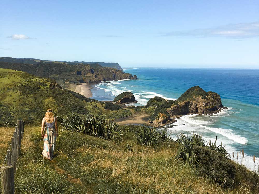 Me walking through an elevated grass covered coastal walk above the blue sea on a clear day in New Zealand.