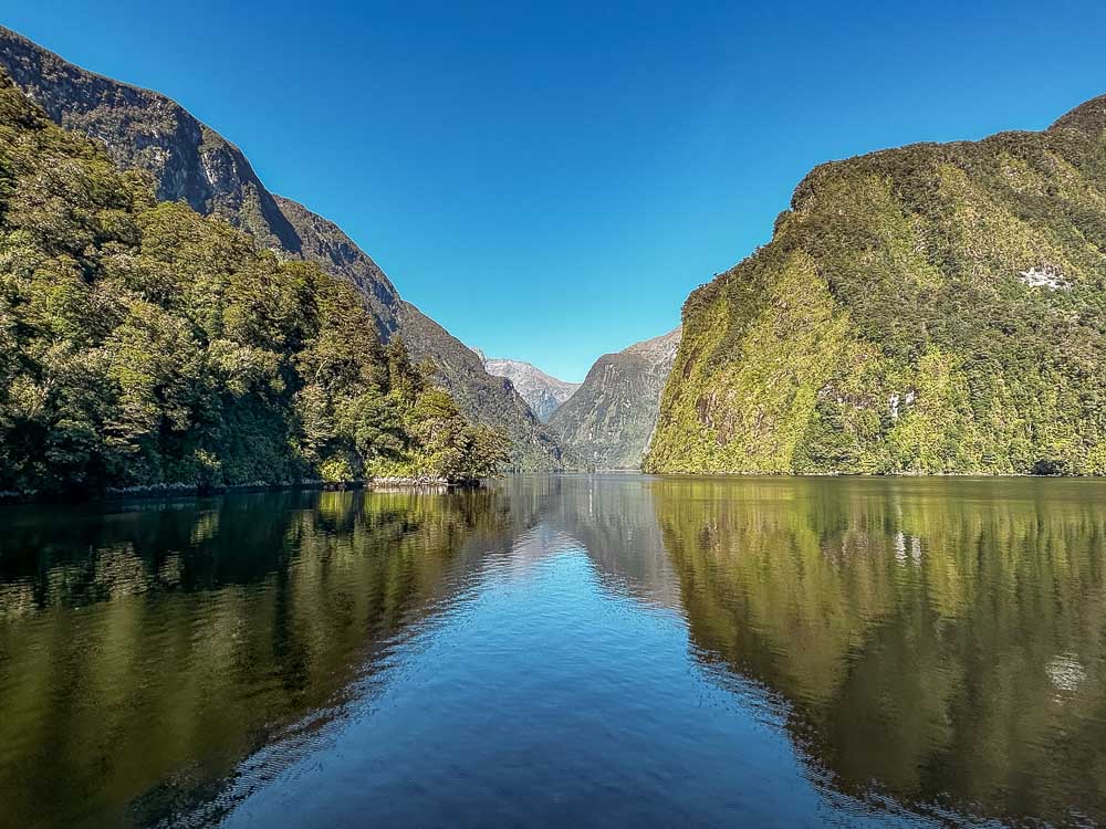Reflections of mountains in water with a clear blue sky in Doubtful Sound New Zealand