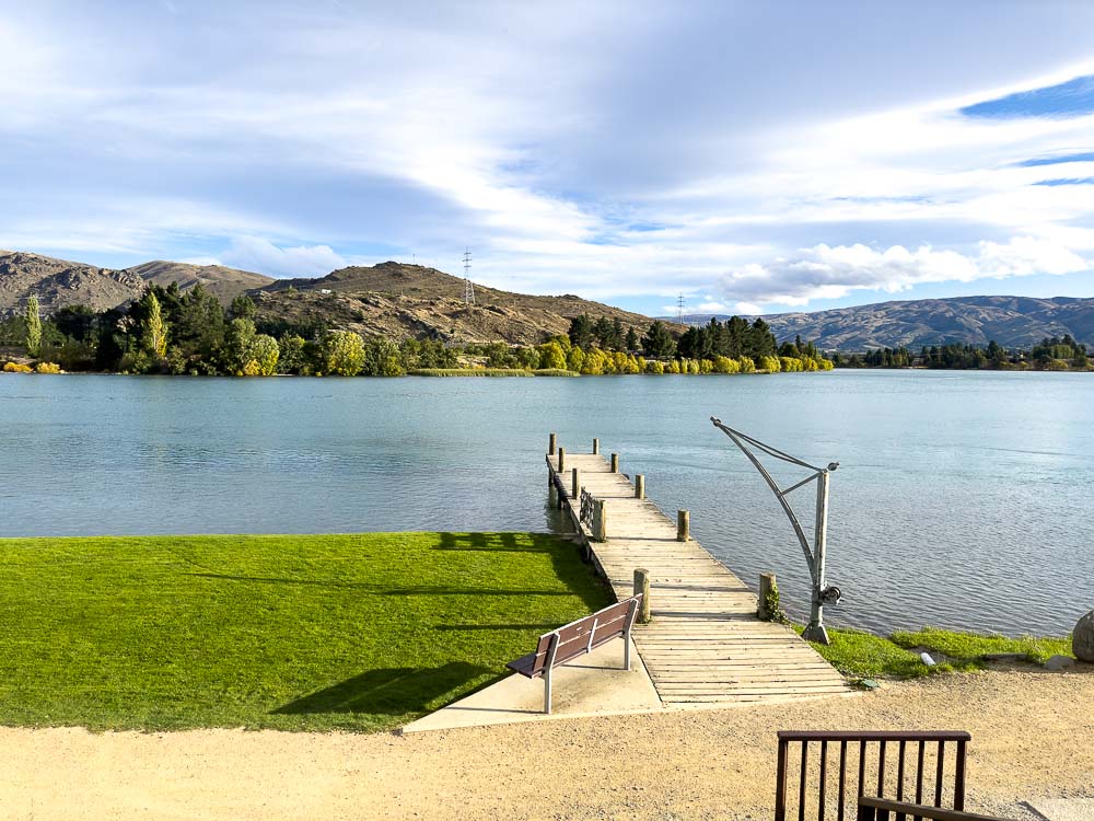 Blue lake Dunstan with green grass in foreground and a dock leading out to the lake