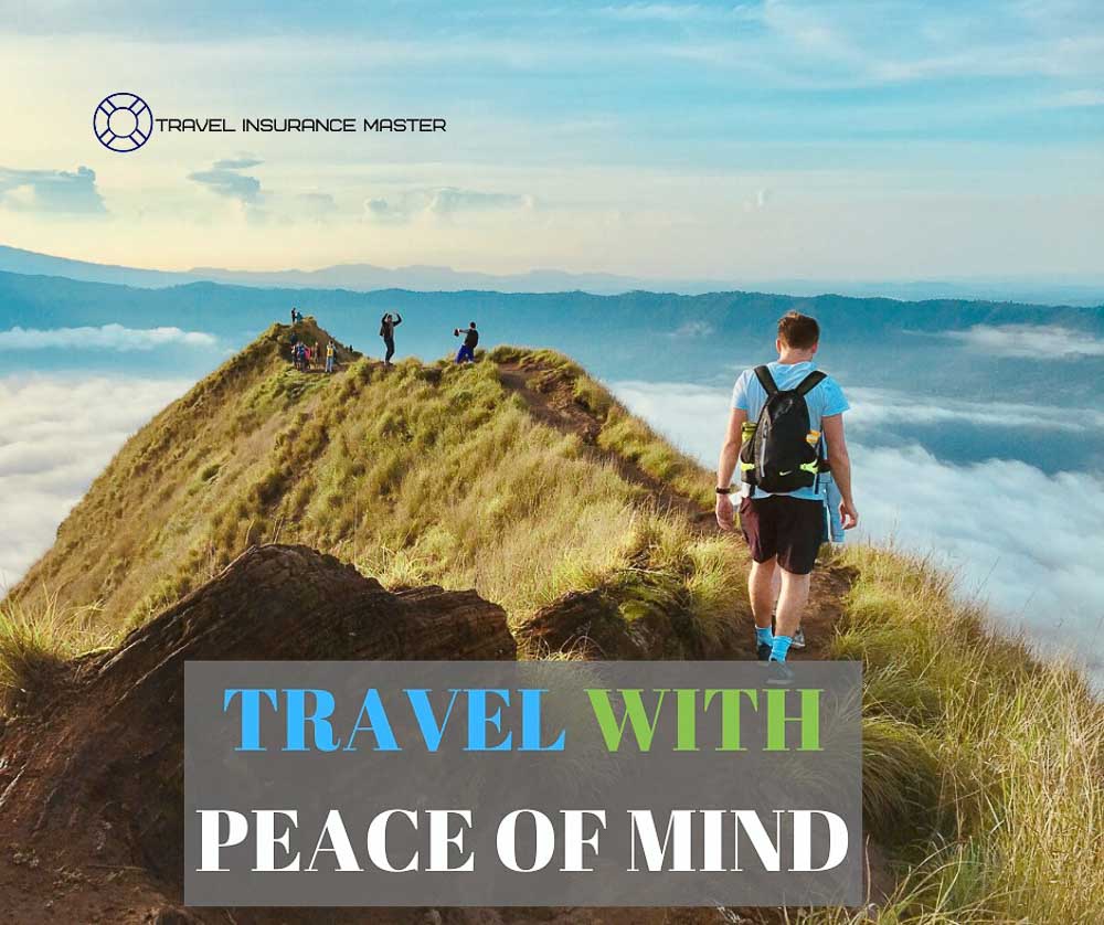 Travel Insurance Master photo of people on a grassy mountain ridgeline above the clouds with a sign the says 'travel with peace of mind'.