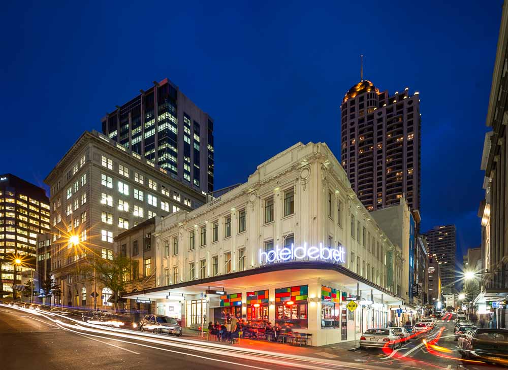 The exterior of Hotel De Brett, a heritage building, at night with colorful glass mosaic lit up on the ground floor Corner Bar.