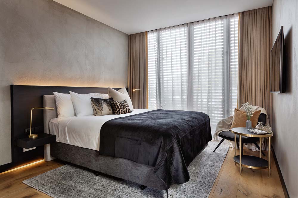 Inside the room of the Hotel Fitzroy in Ponsonby Auckland with wooden floors, a grey throw rug and simple earth tone decor.
