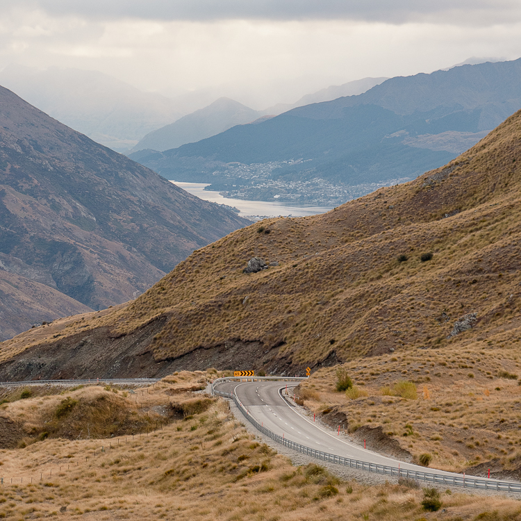 Narrow winding road through the Crown Range with Queenstown in the far distance.
