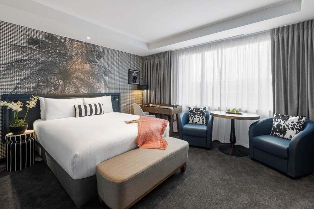 Interior of Imagine Beach Road Hotel Room in Auckland CBD, decorated in grey tones with a white bed and blue chairs.