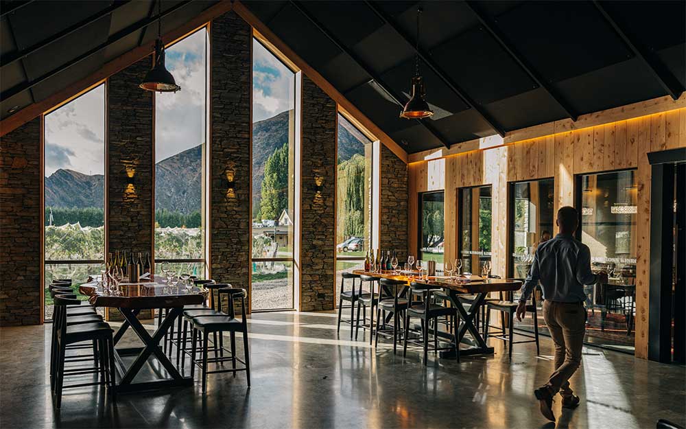 Dark interior of the Kinross Cellar door featuring wood and stone walls and an A frame ceiling featuring full length windows looking out to the mountains and vineyard.