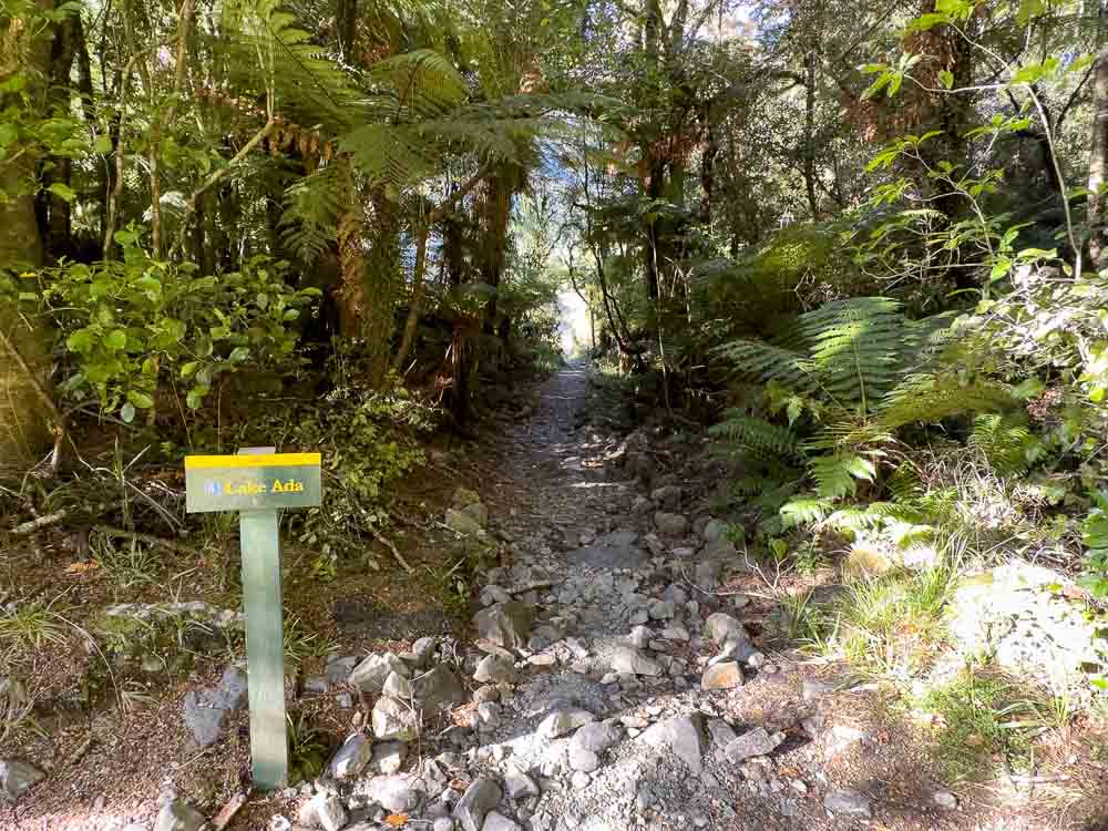 sign saying lake ada with a dirt trail leading into forest