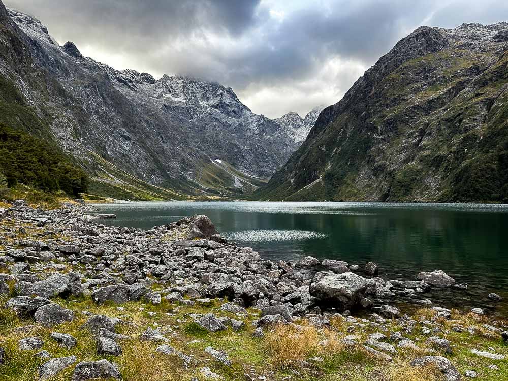 The blue lake marian surrounded by mountains with a rocky shoreline on a cloudy day.