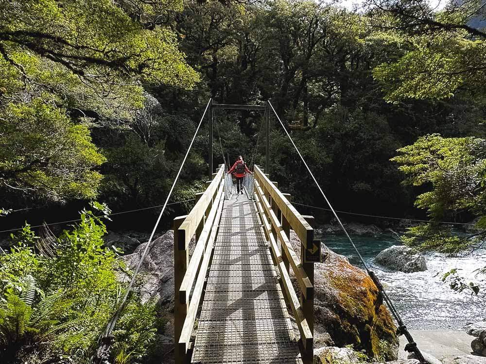 girl walking over a swingbridge on the lake marian track in Fiordland New Zealand.