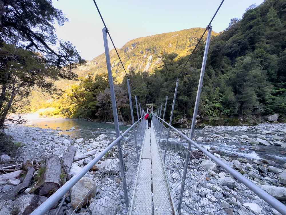 girl walking over a swingbridge with rocks and a river under it