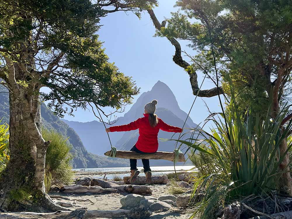 girl in red jacket sitting on a wooden swing with mountain in the background