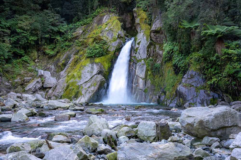 waterfall coming out of rock wall with green trees and moss