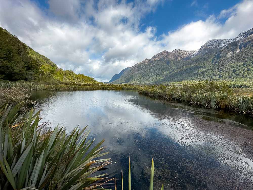 Mountains and clouds reflecting in Mirror Lake on the road to Milford Sound in New Zealand.