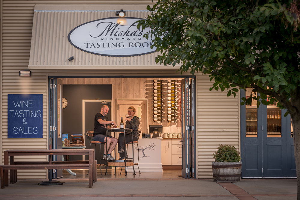 A couple sitting at high table enjoying a wine tasting at Misha's Vineyard tasting room in Cromwell.