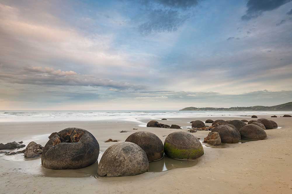 Large spherical boulders scattered along Koekohe Beach in New Zealand at sunset.