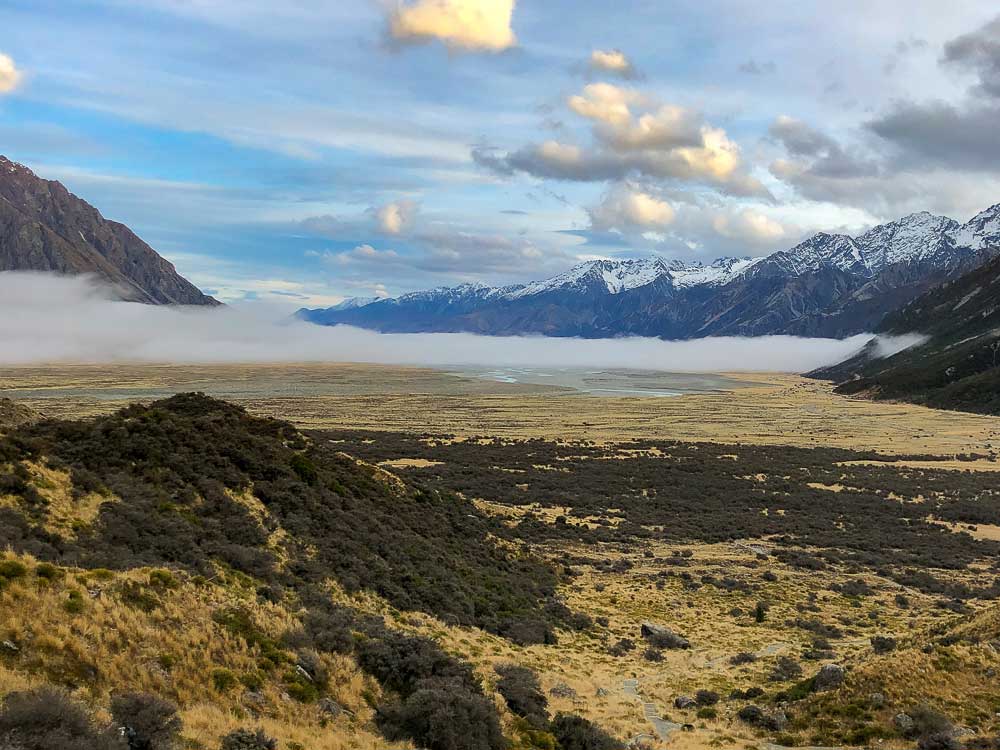 Elevated view over a golden valley with low hanging fog and snow capped mountains in Mt Cook National Park.