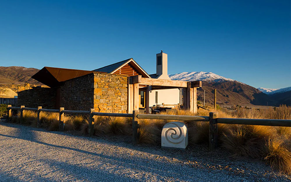 The stone and wood cellar door at Mt Difficulty winery in Central Otago with snow-capped mountains in the background on a clear day.