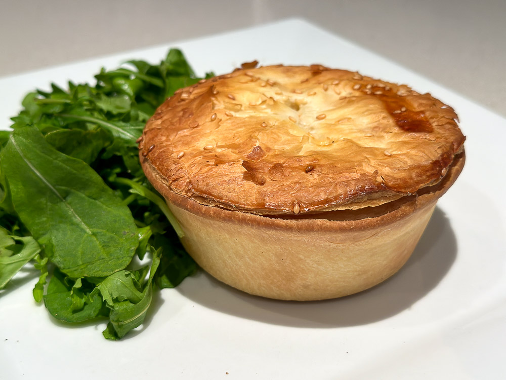 new zealand meat pie and green salad on a white plate.