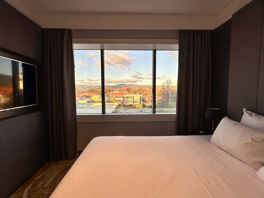 Bedroom at Pullman Rotorua with a large window overlooking the city of Rotorua, New Zealand.