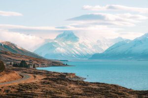 The winding Mount Cook Road running alongside the turquoise colored Lake Pukaki with Aoraki Mt Cook in the distance.