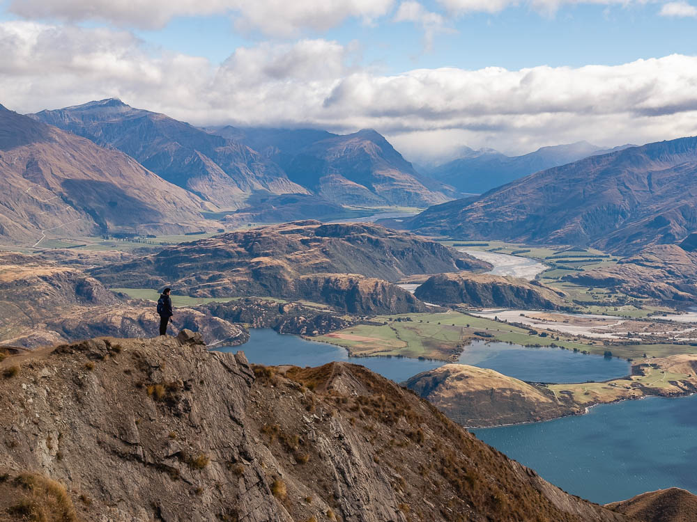 Girl standing on summit of roys peak with lake and mountains in the background.
