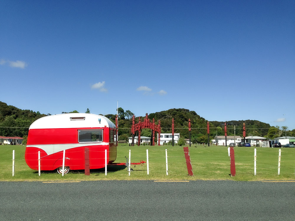 A bright red trailer parked in a green field along the side of a road in rural New Zealand. 