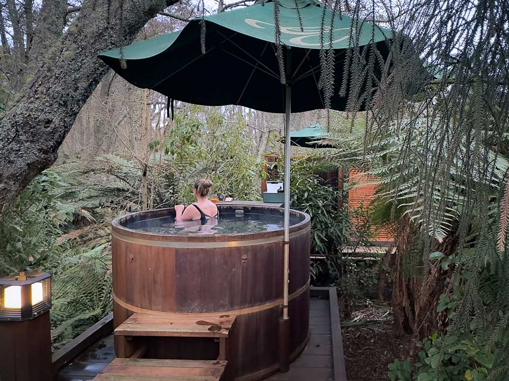 Person relaxing in a cedar hot tub overlooking the forest at Secret Spot Hot Tubs in Rotorua, New Zealand.