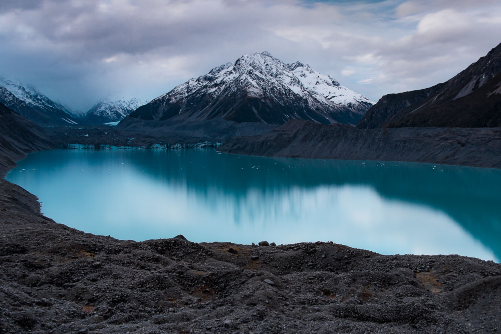 The blue Tasman with snow capped mountains seen from the Tasman Glacier View Track in Mt Cook at sunset.