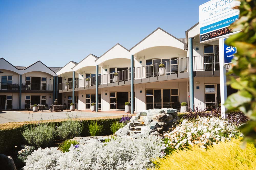 row of 2 story white hotel rooms with a garden in front