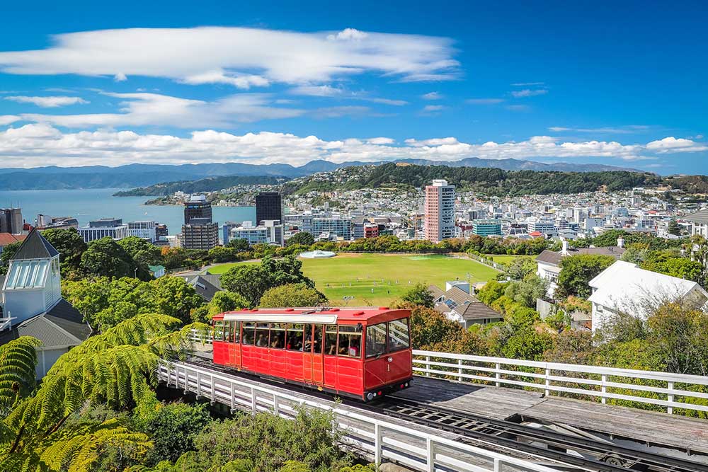 Red Cable Car going up a big hill in Wellington New Zealand with the city and bay in the background. 