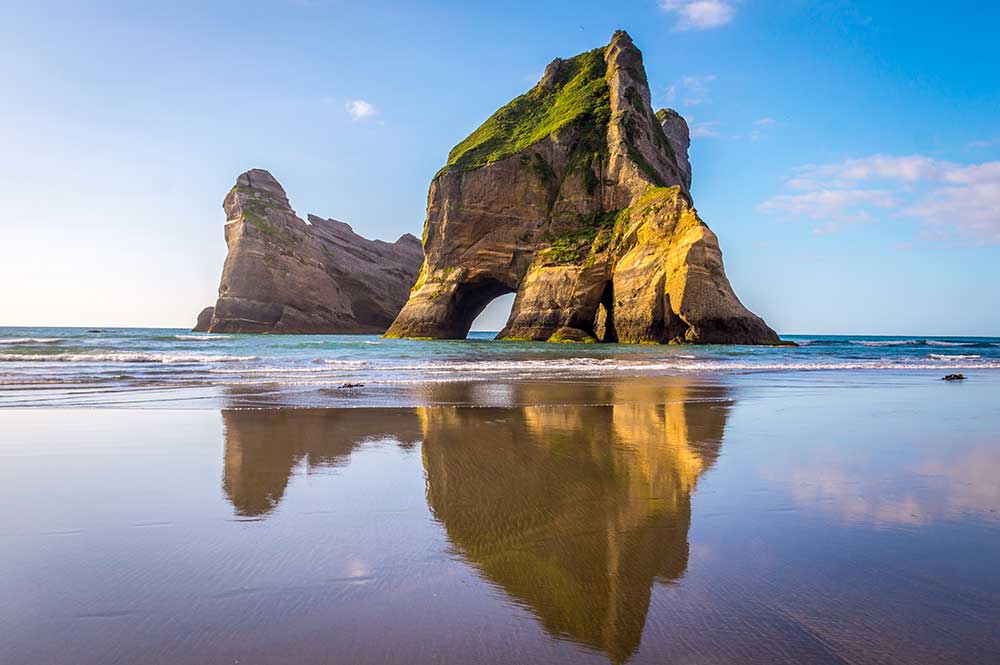 Beautiful rock formations reflected in the glassy sand of Wharariki Beach in New Zealand.
