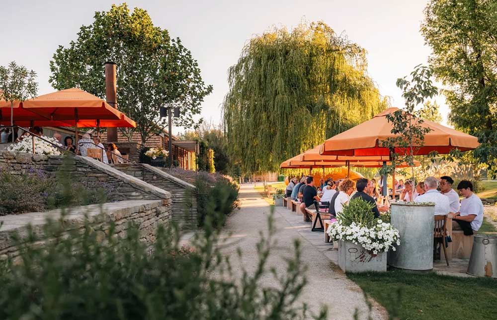 People enjoying outdoor dining under orange unbrellas in a garden setting at Ayrburn Winery near Queenstown.